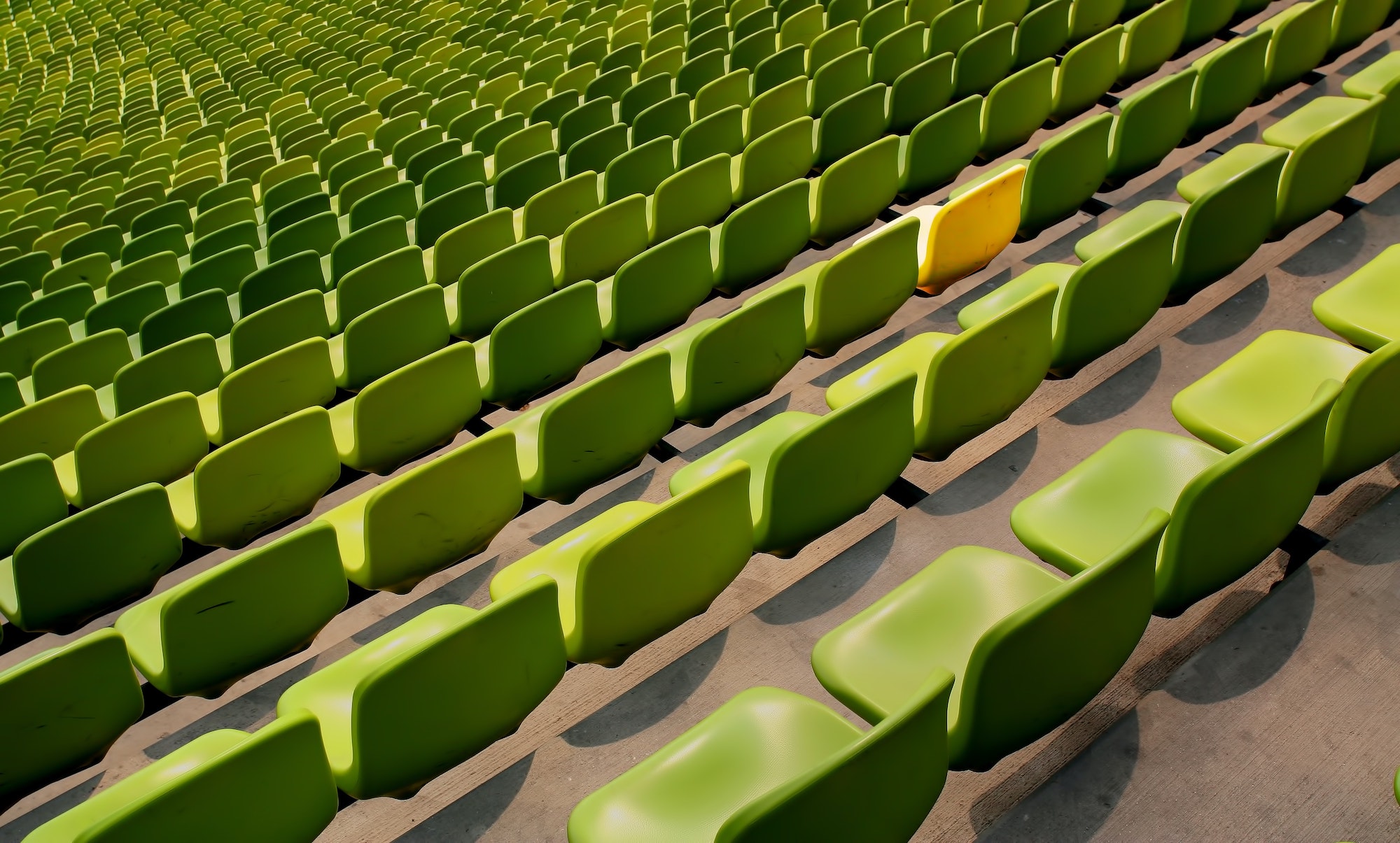 sea of green chairs with one yellow chair, concept of standing out